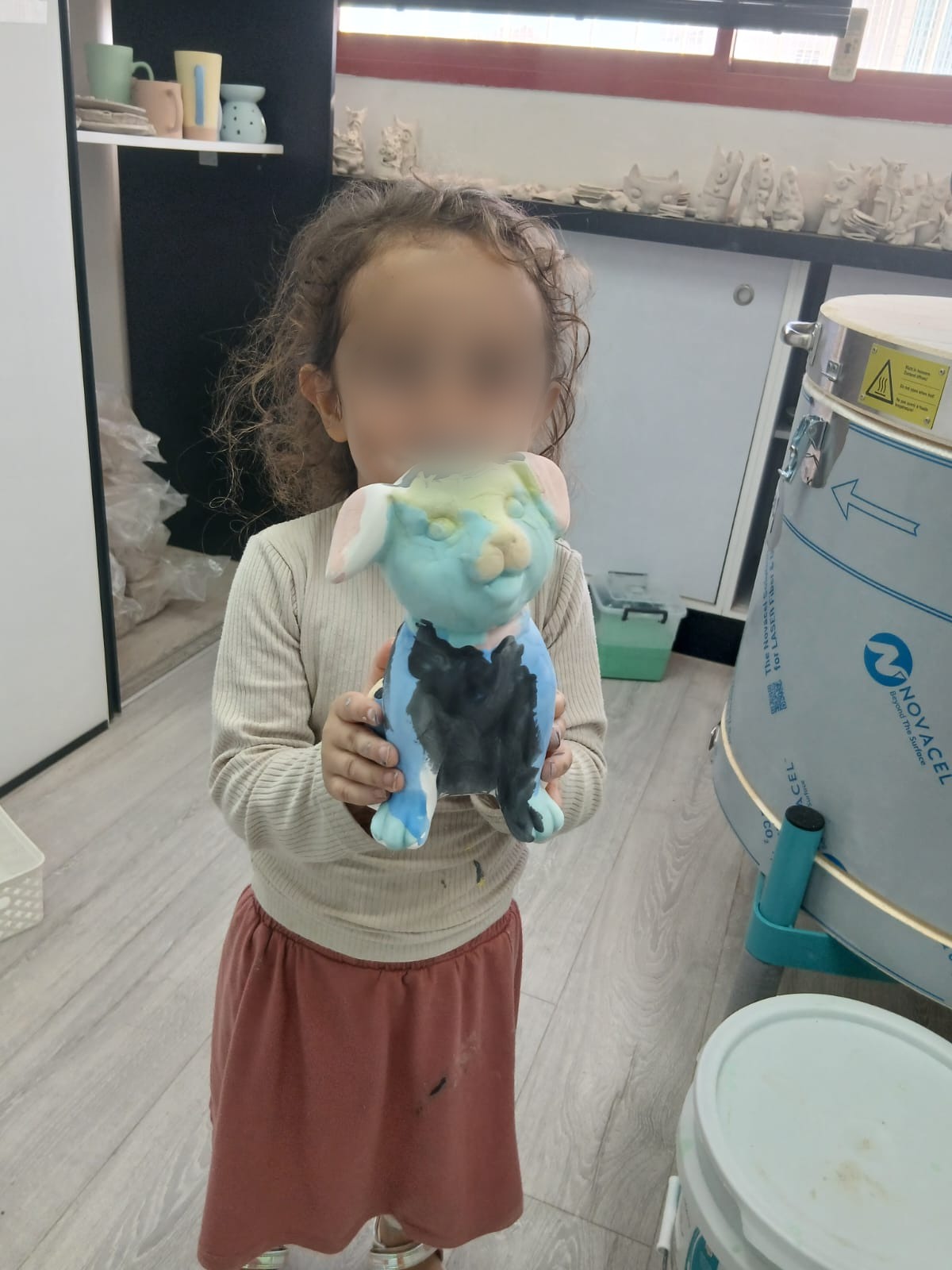 ילדה מחזיקה בגאווה את פסלון הכלב הצבעוני שיצרה בסטודיו