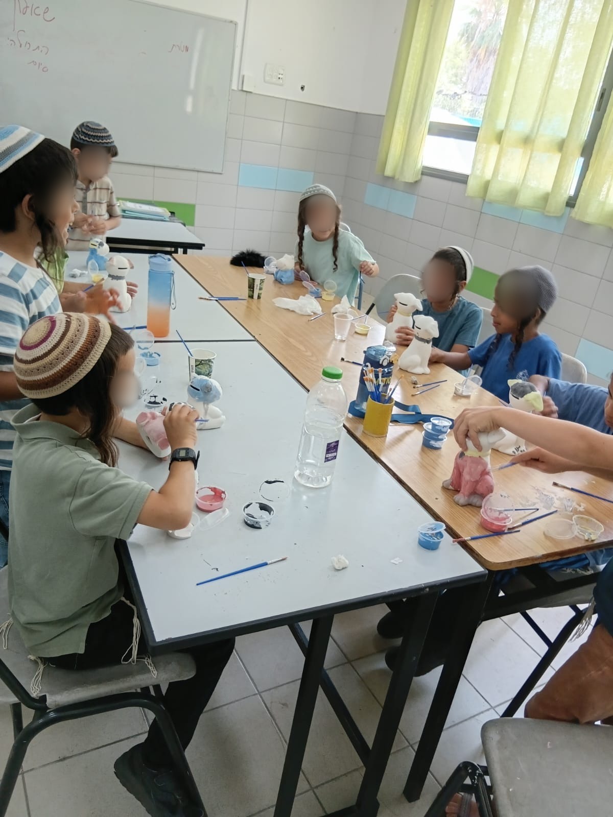 ילדים יושבים סביב שולחנות וצובעים פסלוני קרמיקה בחוג