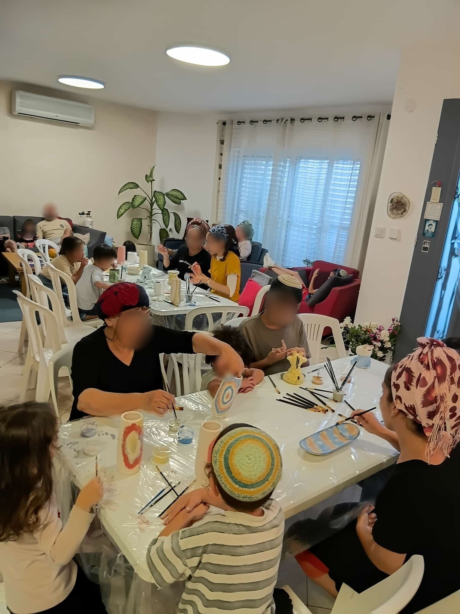 משפחה מרובת דורות יושבת סביב שולחן בסלון וצובעת כלי קרמיקה